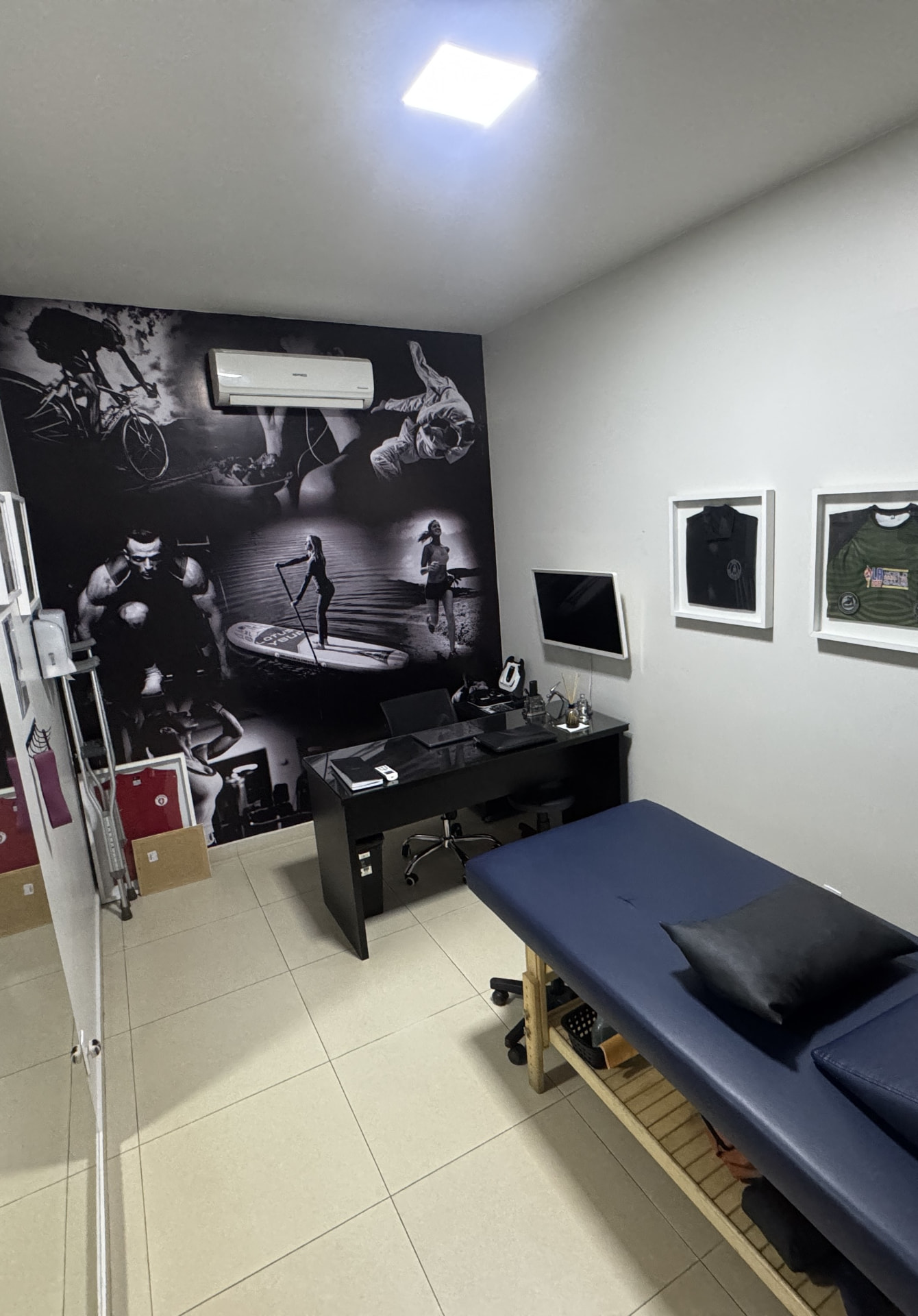 Sala de atendimento da Return to Play com maca, escrivaninha e painel fotográfico esportivo na parede
