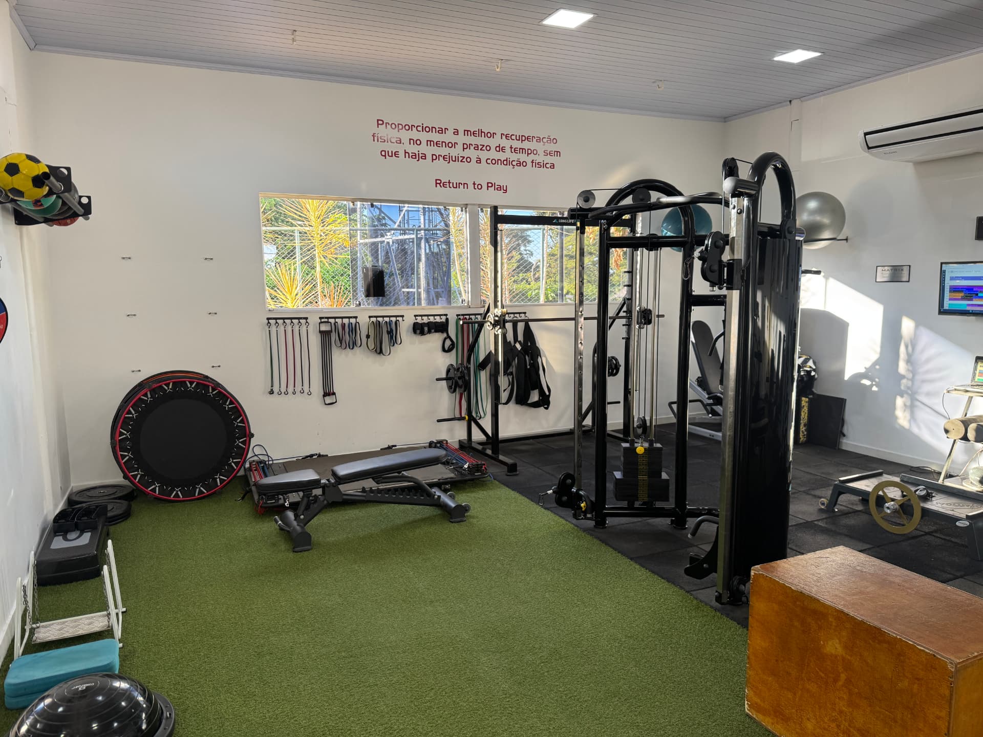 Sala de treinamento da Return to Play com equipamentos de musculação, funcional e faixa na parede