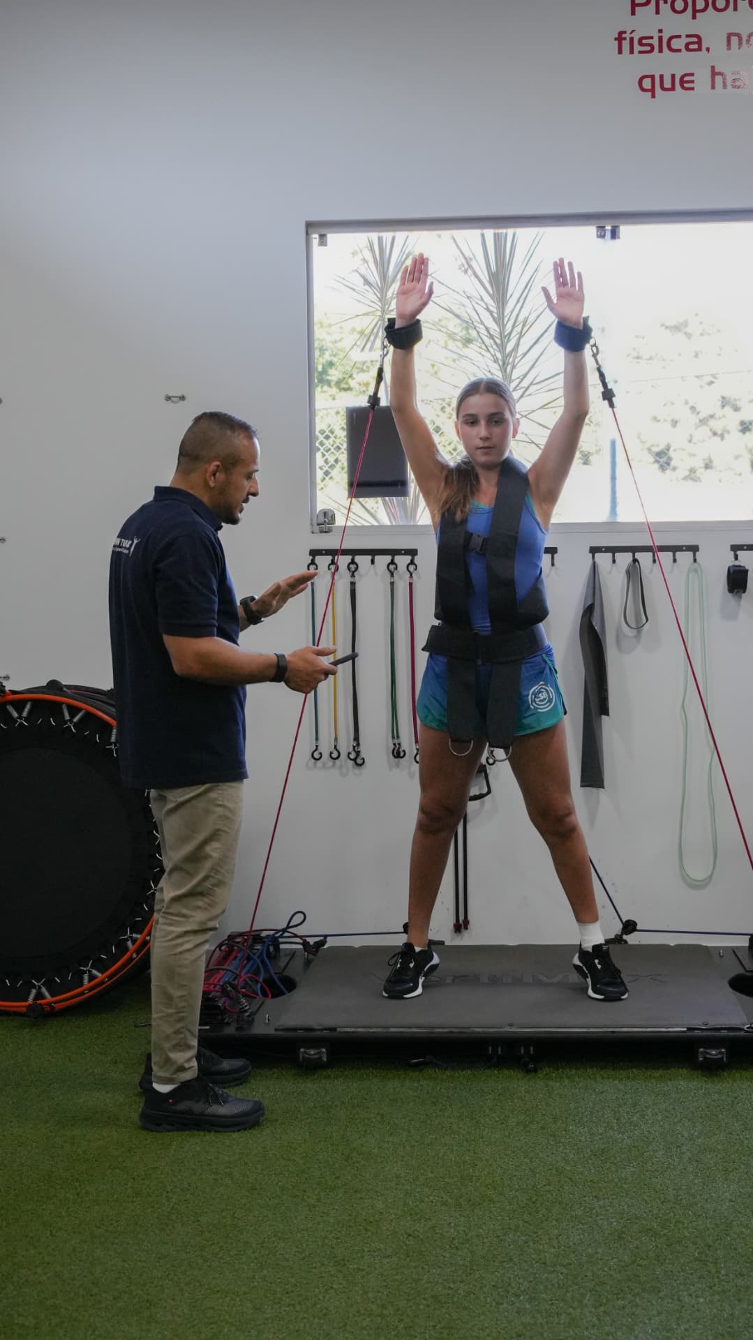 Fisioterapeuta da Return to Play conduzindo sessão de reabilitação funcional com atleta em equipamento de suporte